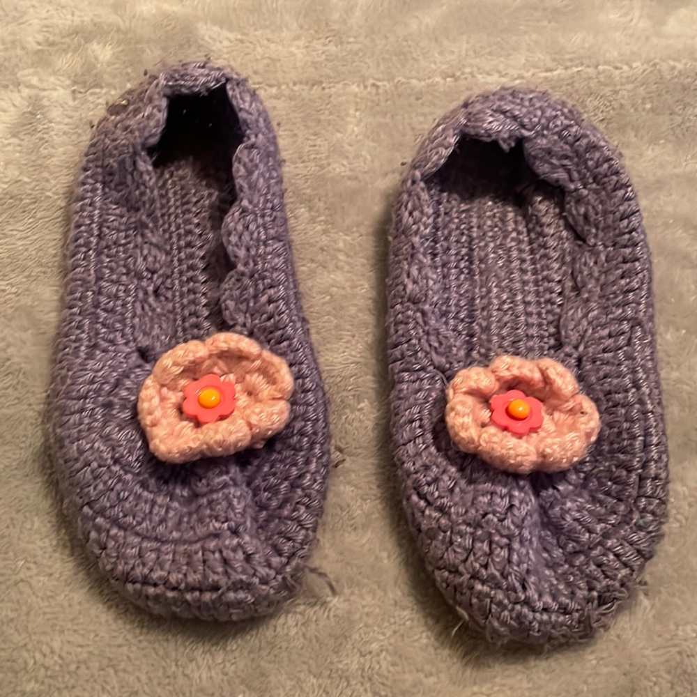 Hand knitted purple slippers with pink knit flower and decorative button.